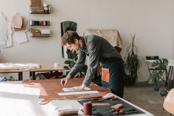 An artisan shaping leather by hand at a sunlit workshop table